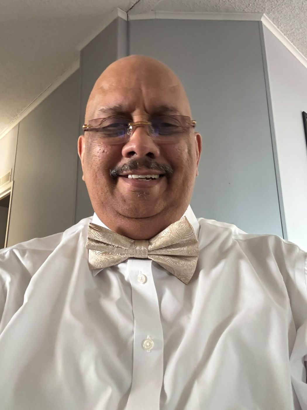 Man in white dress shirt and gold bow tie wearing glasses, smiling at camera