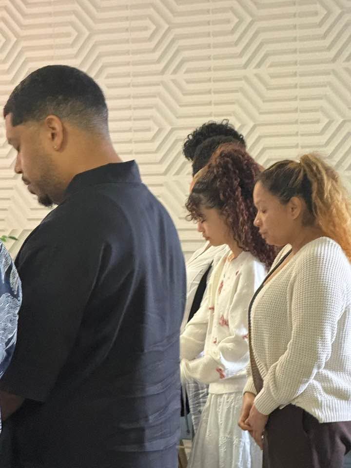 Four people standing together indoors against a geometric patterned wall