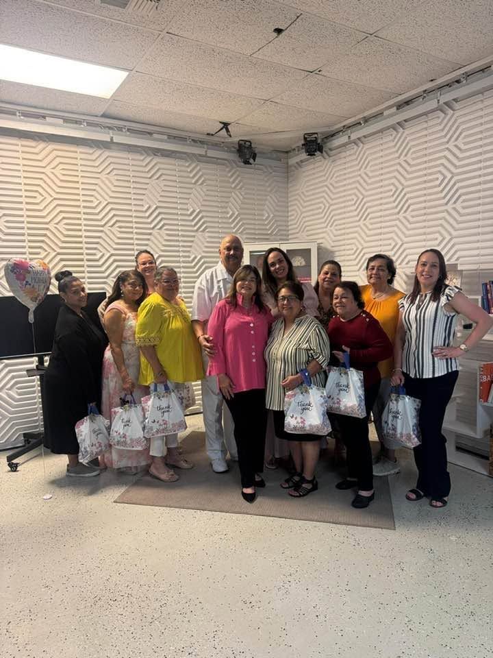 Group of people holding gift bags posing together in an indoor room with geometric wall patterns