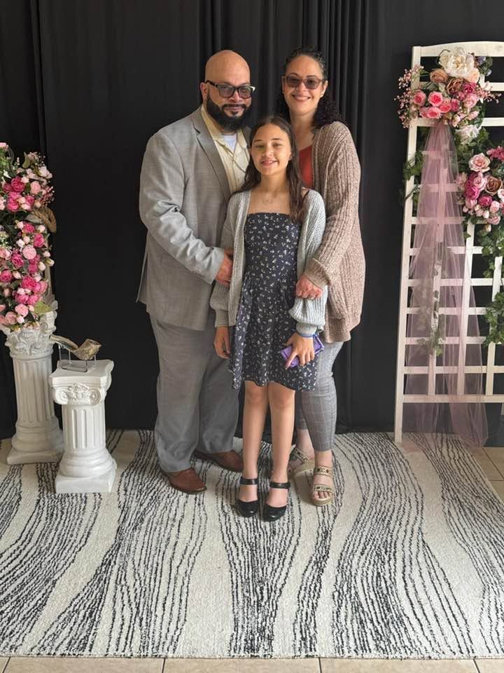 Family of three posing in front of floral arrangements and decorative columns