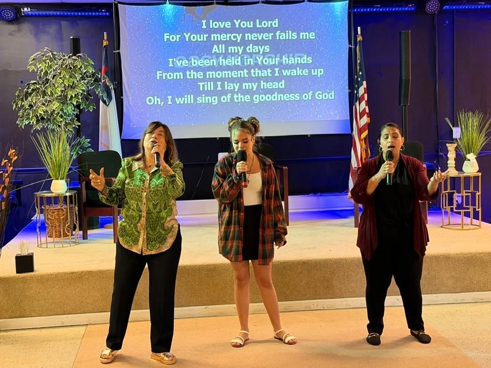 Three women singing with microphones on stage during a worship service
