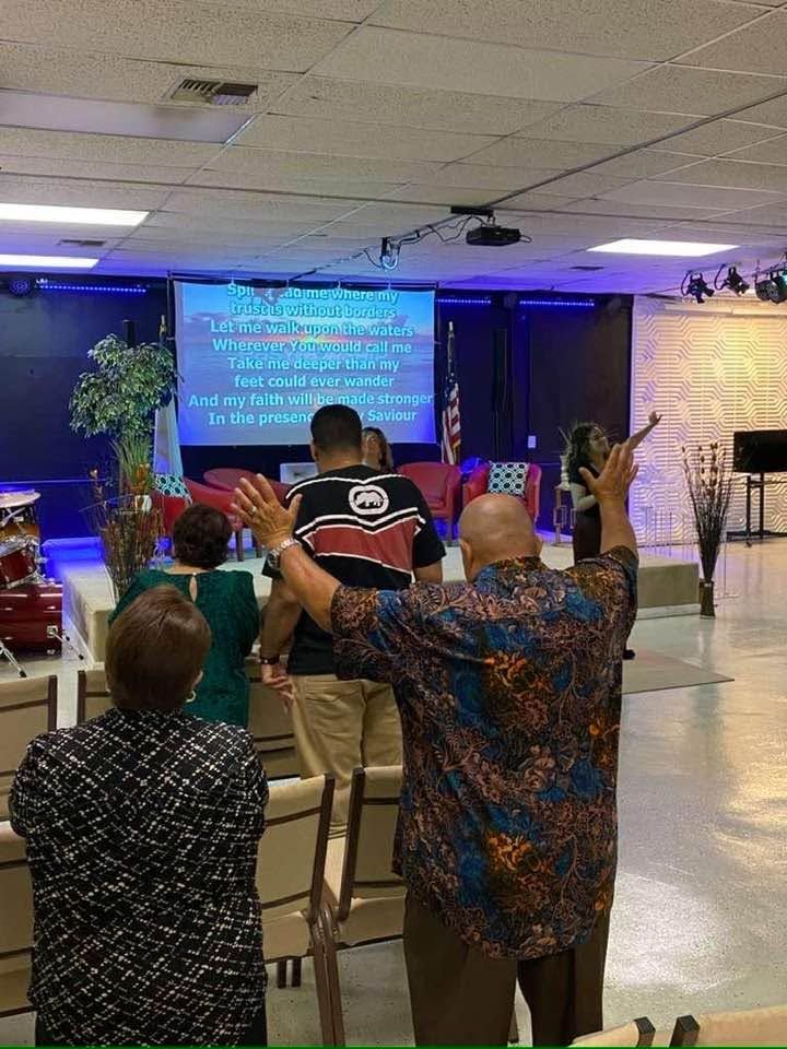 Congregation members with raised hands during worship service with lyrics displayed on screen